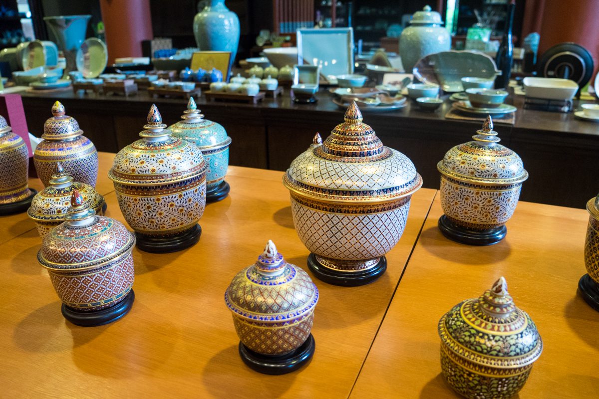 A collection of intricately patterned ceramic jars with lids displayed on a wooden table, possibly in a shop or museum with various ceramics in the background.