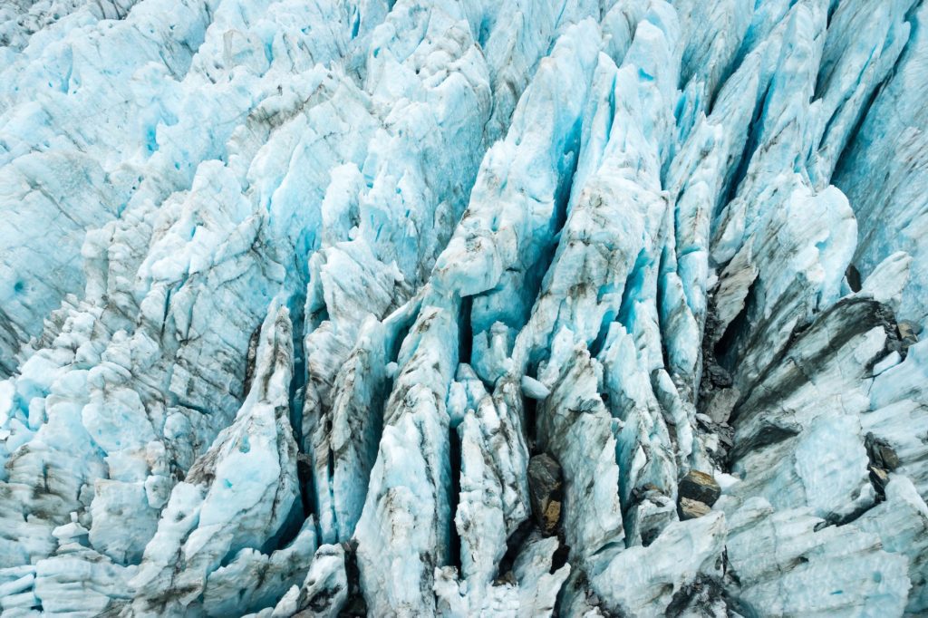 This image shows the rugged surface of a glacier, with various shades of blue and white ice interlaced with dark crevasses and dirt inclusions.