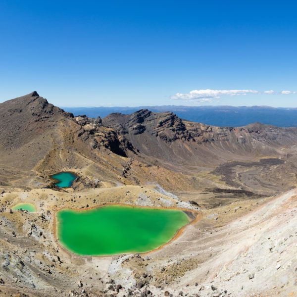Panoramic view of a rugged landscape featuring two vividly colored lakes nestled within mountainous terrain under a clear blue sky.