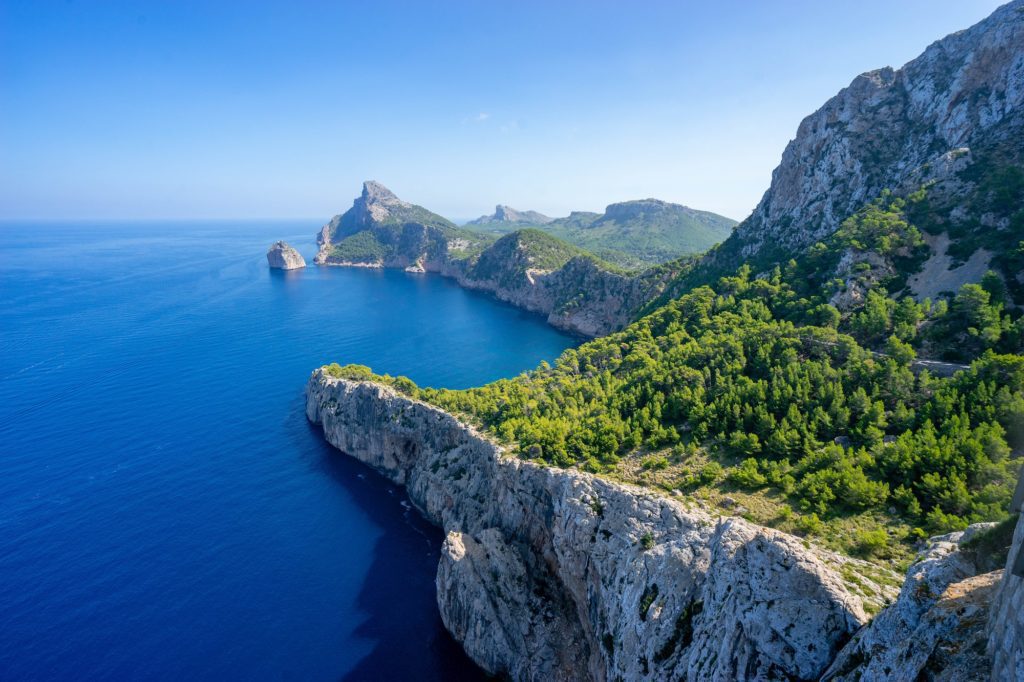 The image shows a stunning coastal landscape with towering cliffs, lush greenery, and deep blue sea under a clear sky. It's serene and picturesque.