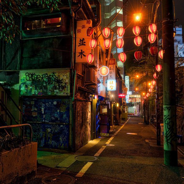 An atmospheric night scene on an urban alley with red lanterns. Graffiti on walls, Asian signage, and a glimpse of a cityscape in the background.