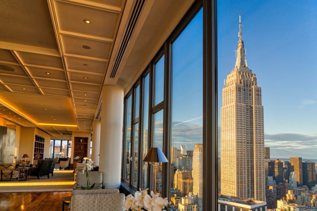 Luxurious interior with large windows offering a stunning view of the Empire State Building during sunset, elegant furnishings, and warm, inviting lighting.