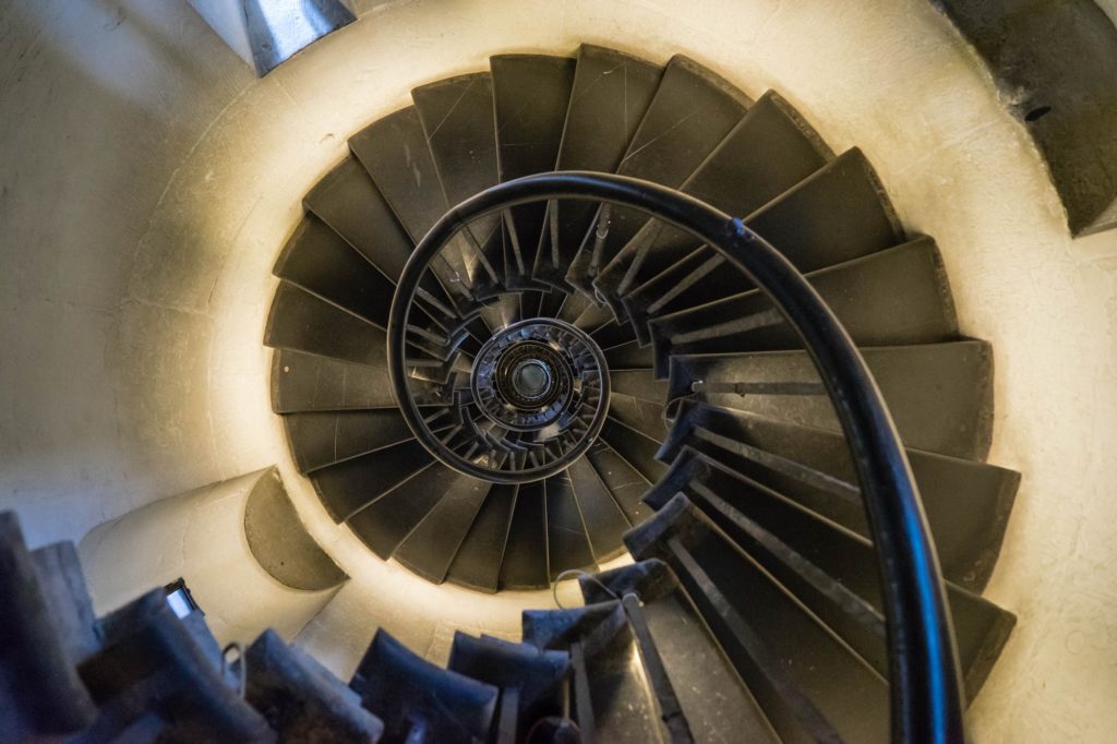 The image captures a spiral staircase from a high angle, creating a hypnotic effect as it twists downwards to its vanishing point at the center.