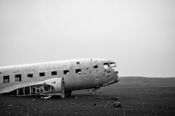 An abandoned airplane fuselage sits on barren terrain under a hazy sky. Monochrome image. The aircraft appears old and weathered, devoid of wings.
