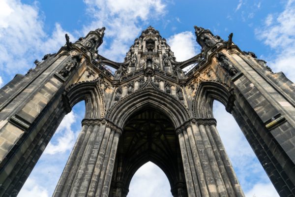 An imposing Gothic-style monument with intricate architecture towers against a partly cloudy sky, showcasing flying buttresses and elaborate stone carvings.