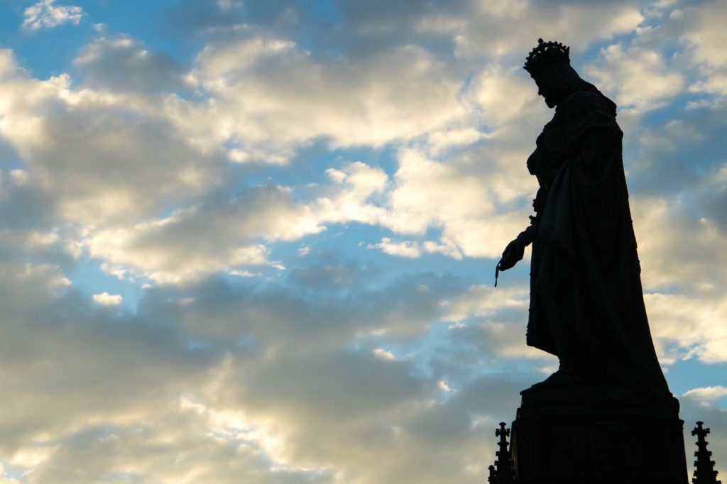 A statue silhouette against a vibrant sky with scattered clouds. The dynamic light hints at either sunrise or sunset. The statue seems regal and poised.
