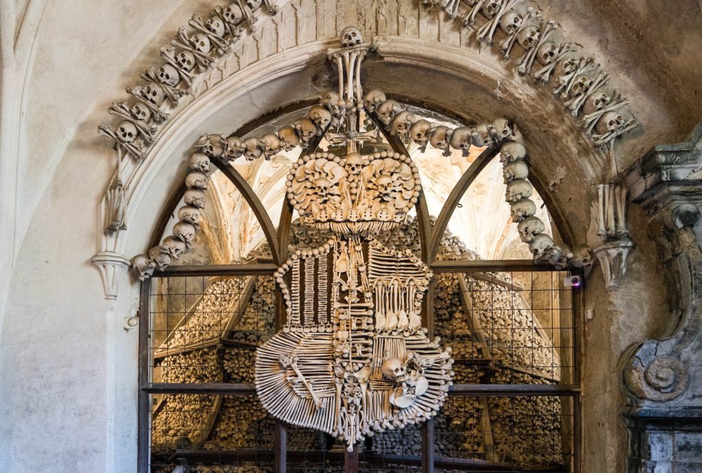 An ornate chandelier made of bones hangs inside an archway adorned with more bones; a representation of a macabre artistic expression within a possibly historic site.