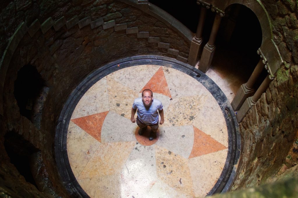 A person is crouching at the base of an ornate circular well with a star pattern on the ground, looking up towards the camera.
