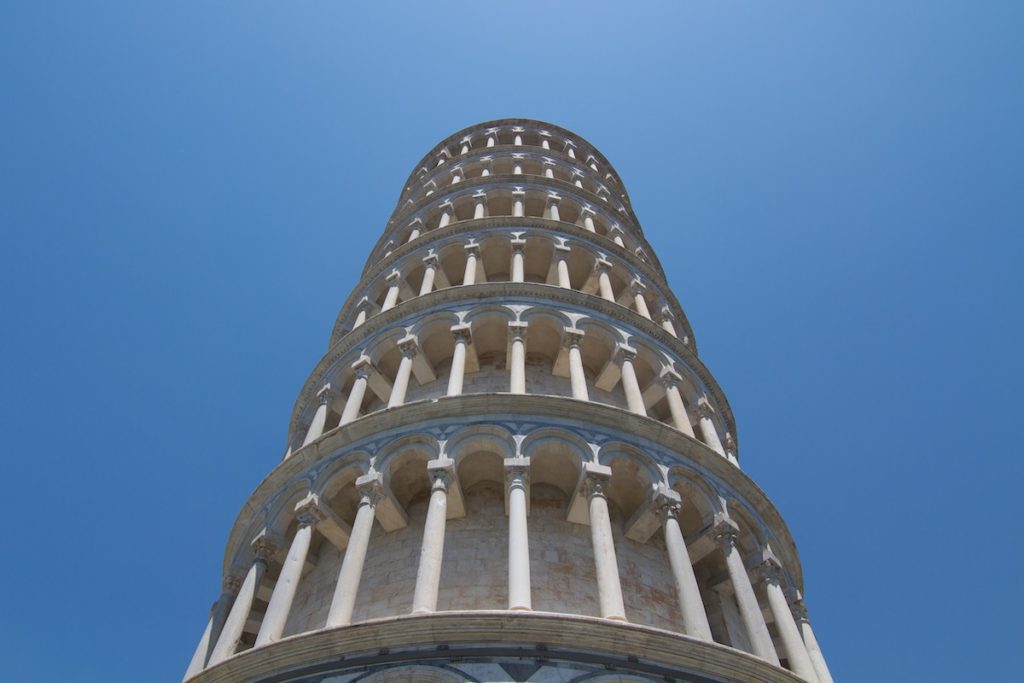 This image shows the upper part of the Leaning Tower of Pisa against a clear blue sky, emphasizing its cylindrical structure and leaning posture.
