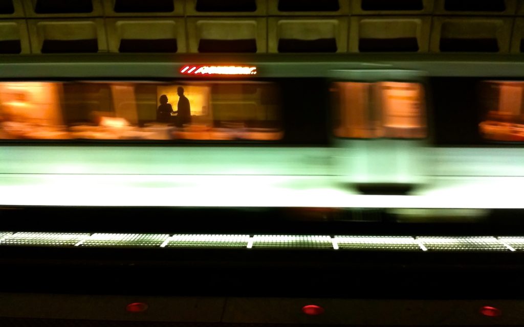 A blurred metro train moves swiftly through a station, featuring dynamic lighting and visible passengers inside. The setting suggests urban underground transit in motion.