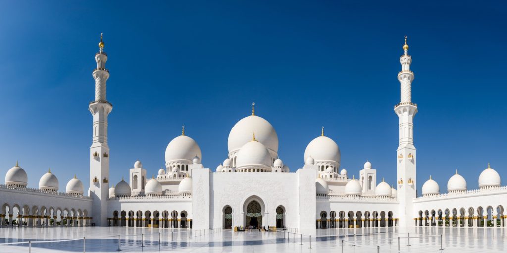 This image shows the Sheikh Zayed Grand Mosque in Abu Dhabi, characterized by its pure white domes, minarets, and an expansive courtyard under a clear blue sky.
