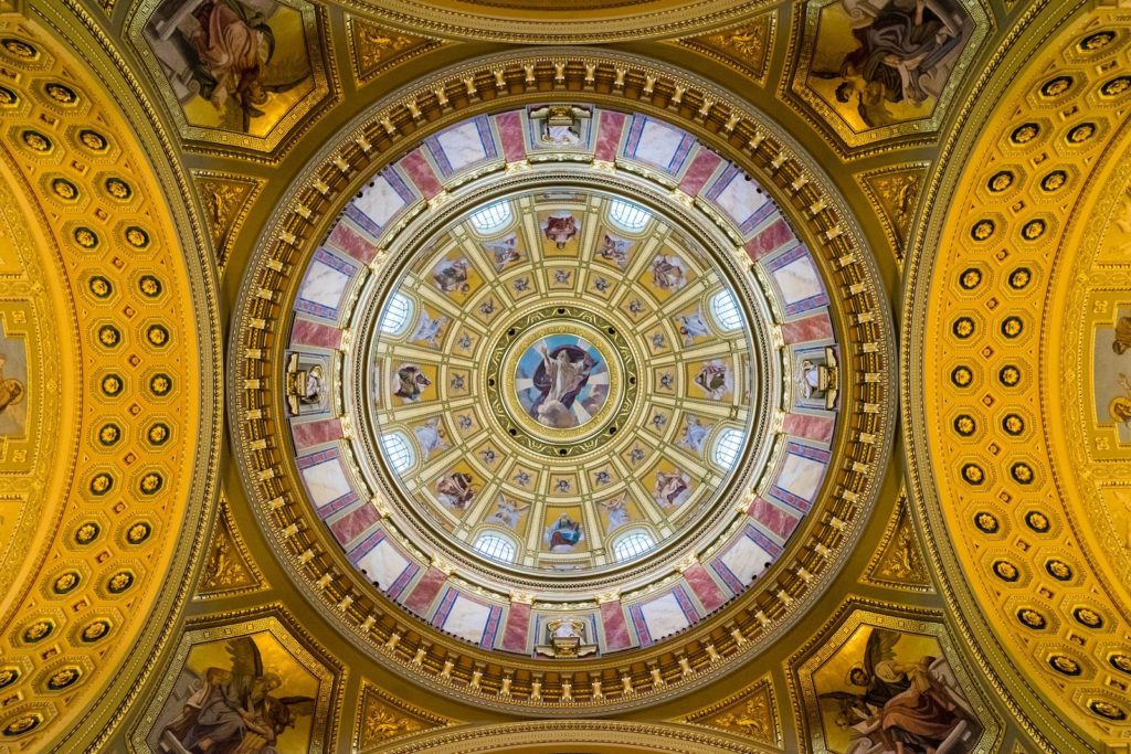 The image features a detailed dome ceiling with intricate frescoes, gold detailing, and architectural elements in a circular symmetrical pattern with soft natural light.