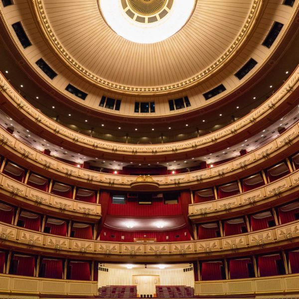 A grand theater interior with multiple ornate balconies, red seats, a decorative ceiling, and an empty stage. It appears opulent and traditional in design.