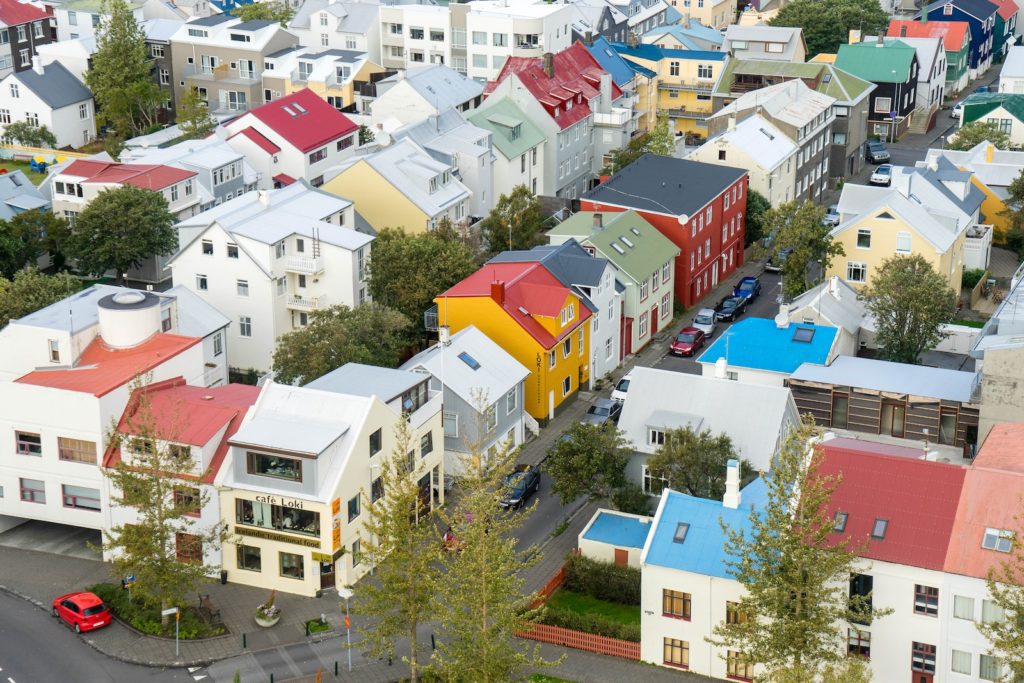 This image shows an aerial view of a quaint urban area with colorful houses and buildings, trees, and cars along the streets.