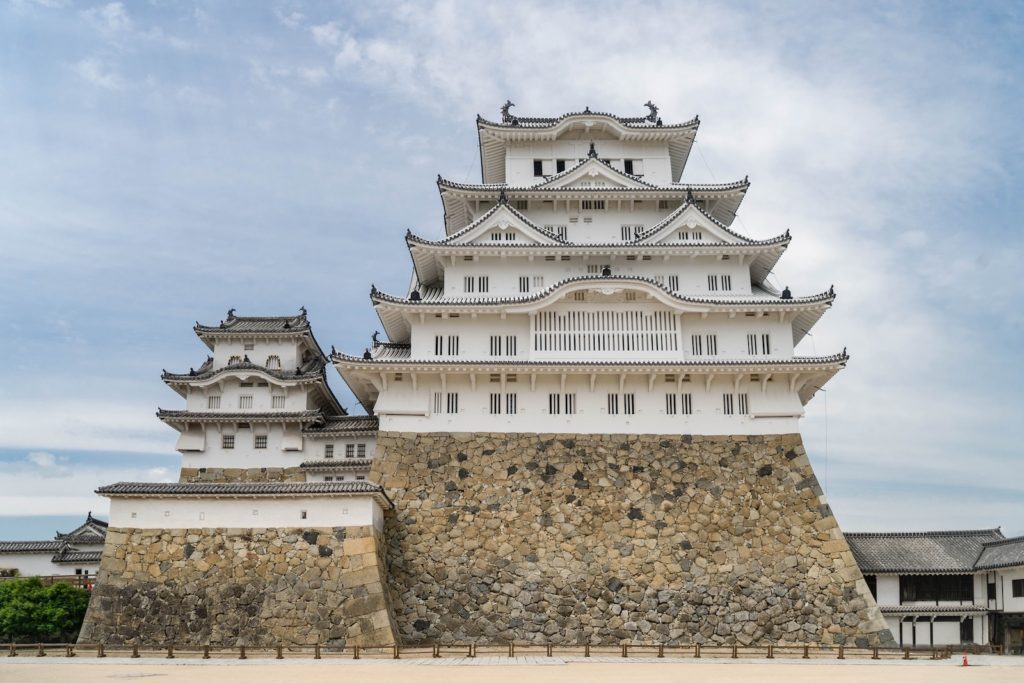 This is a photo of the historic Himeji Castle in Japan, showcasing its intricate white façades and traditional wooden architecture atop a stone base under a cloudy sky.