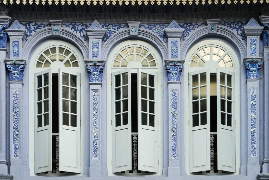 The image shows three arched white doors set in a blue and white patterned facade, typical of colonial architecture, possibly from Southeast Asia.