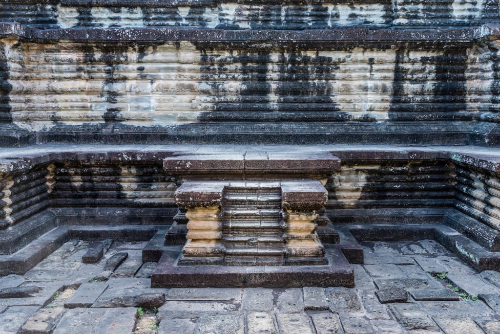 This image shows an ancient, weathered stone structure with symmetrical steps leading to a platform, reminiscent of traditional architecture from historical sites.