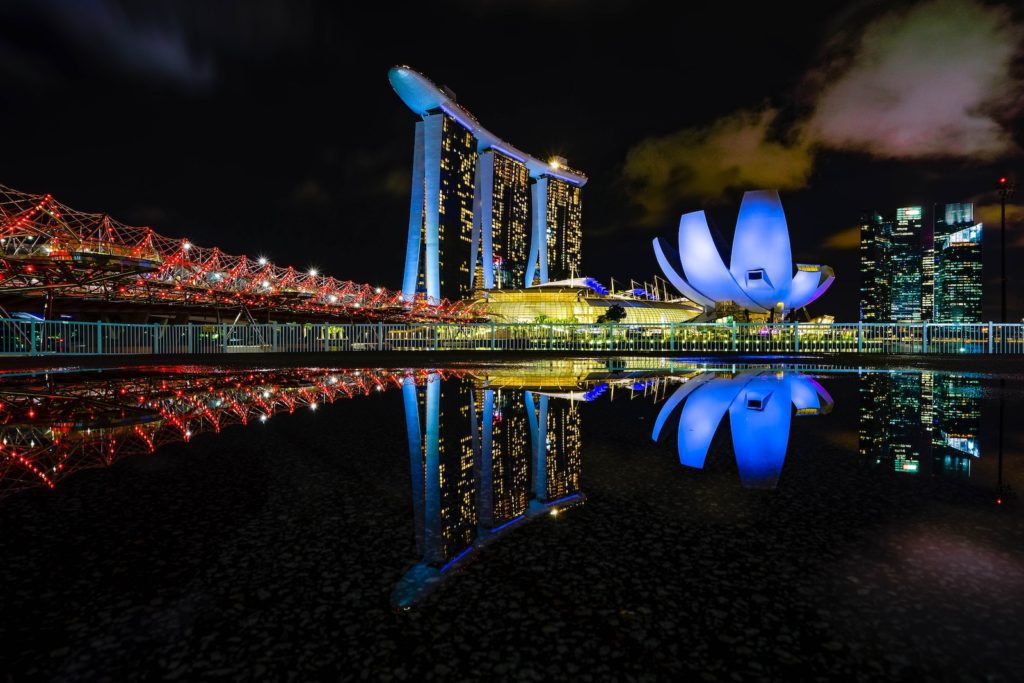 The image features Singapore's iconic Marina Bay Sands hotel and the Helix Bridge at night, with a striking reflection on the water's surface.