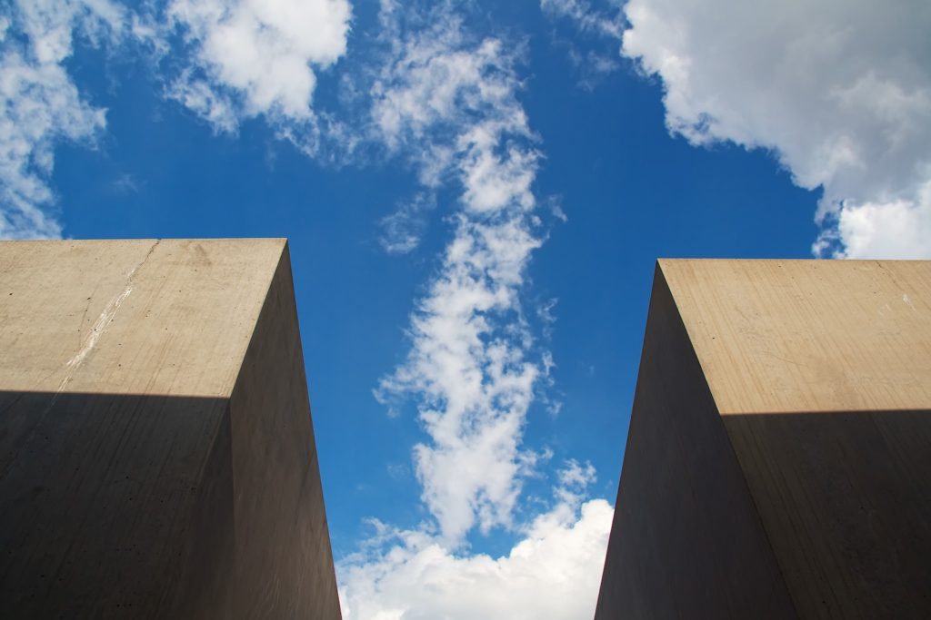 The image shows a view looking upwards, framed by two tall, concrete structures on each side against a blue sky scattered with white clouds.