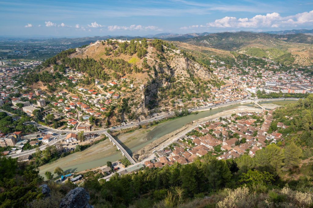 This is an aerial view of a town nestled in a valley with a river cutting through it, surrounded by hills and a prominent rocky outcrop.