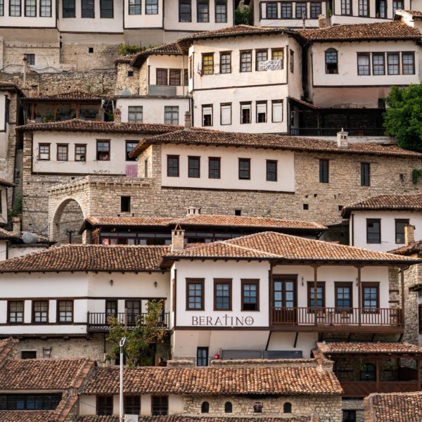 A dense cluster of traditional houses with terracotta roofs and white walls built on a hillside. A sign marked "Beratino" is visible on one building.
