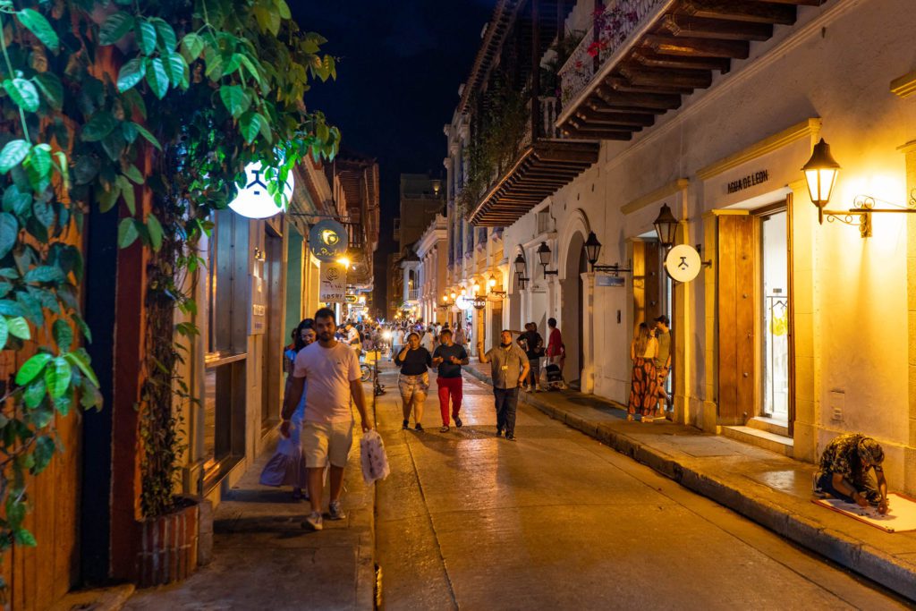 This image shows a bustling evening street scene with people strolling, colonial architecture, warm lighting from shops, and a vibrant, cozy atmosphere.