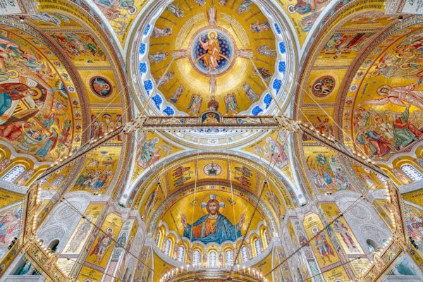 Ornate religious interior with golden domes and arches featuring elaborate frescoes and icons. Central figure of Christ Pantocrator dominates the apse. Bright and detailed artwork.