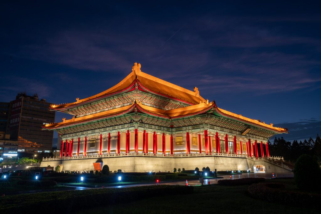 Illuminated National Concert Hall in Taipei, Taiwan, at night. Traditional Chinese architectural style with ornate details and vibrant colors. Cityscape in the background.