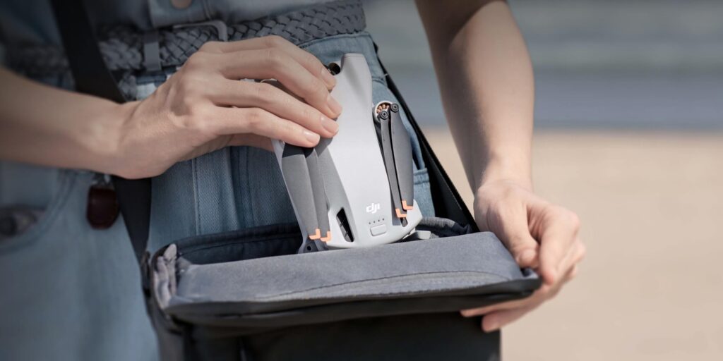 A person is putting a small drone into a gray carrying case, with the focus on the hands and the device.